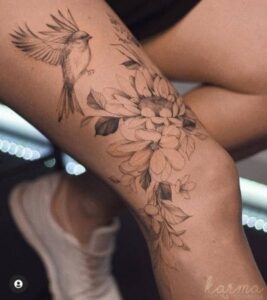 Tatuagem feminina na coxa floral com pássaro, delicada.