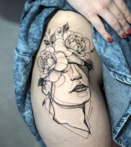 Tatuagem feminina na coxa metade rosto e metade flores.
