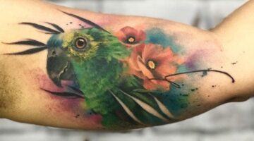 Tatuagem em aquarela, papagaio com flores num galho.