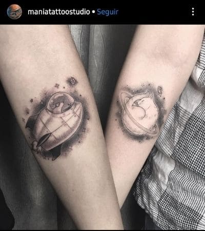 Tatuagem de casal com o desenho de um gato em forma de planeta e um gato pilotando uma nave.