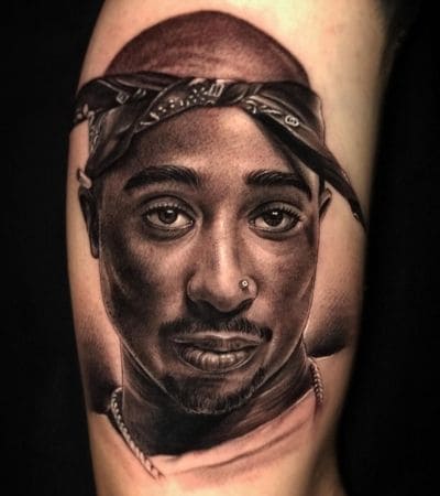 Tatuagem realista, retrato do rapper 2Pac em preto e cinza.