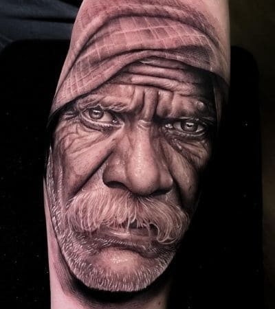Tatuagem realismo do retrato do rosto de um senhor em preto e cinza.
