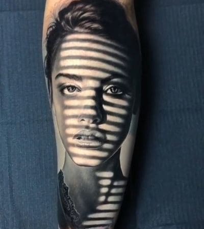 Tatuagem realismo retrato do rosto de uma mulher, parte coberto por sombras.