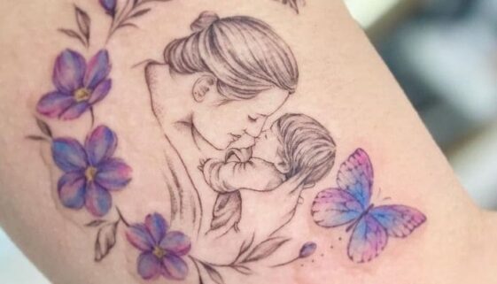 Tatuagem para homenagear filhos, mãe segurando seu bebê com flores e borboletas coloridas ao redor