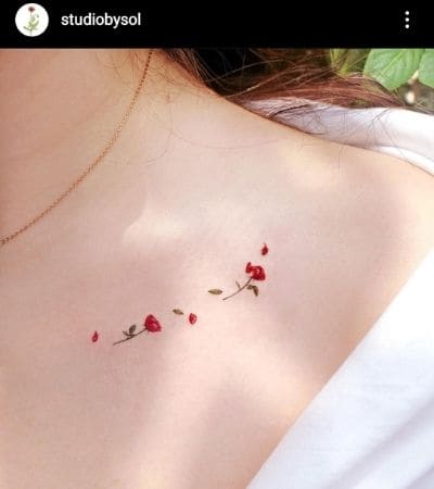 Tatuagem minimalista de uma rosa vermelha soltando pétalas, feita na clavícula.